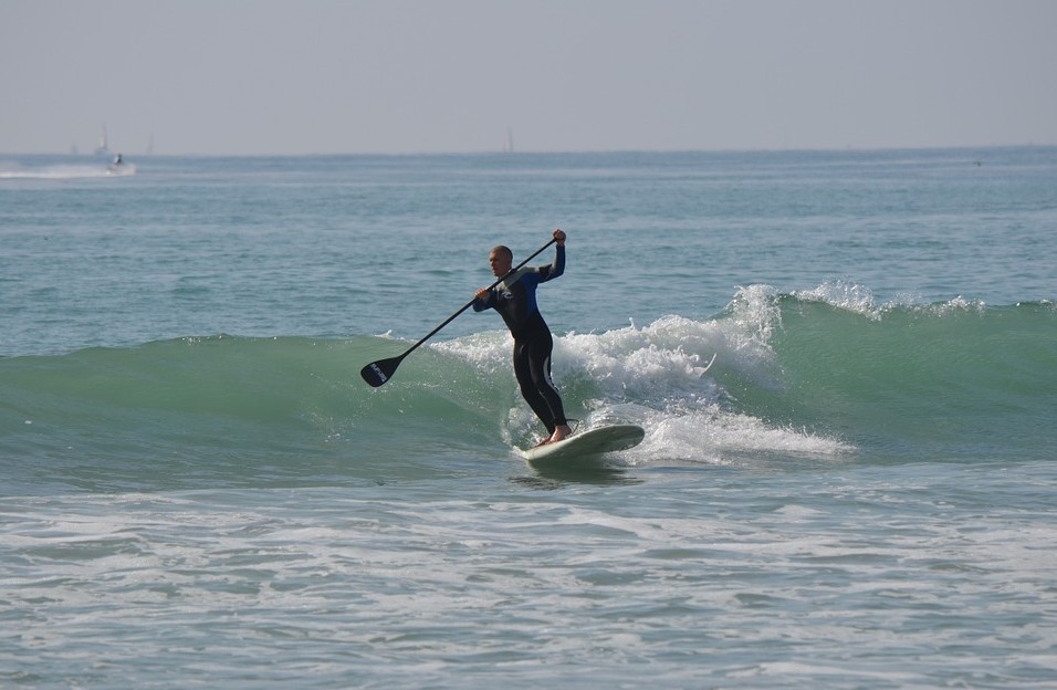 A man in black balancing on the paddleboard, stand-up paddleboarding, ocean