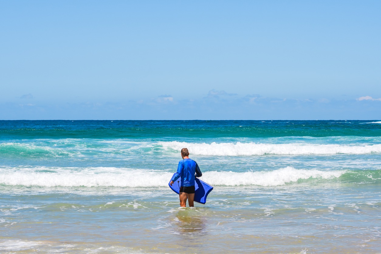 Young man enters the sea with bodyboard, doing water sport