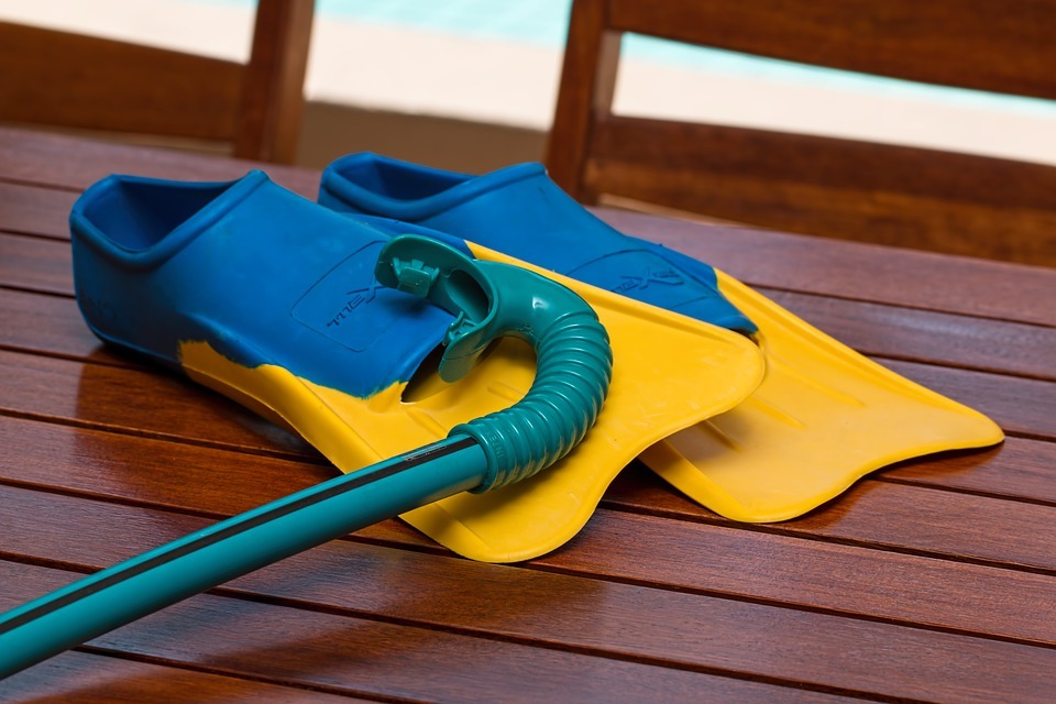  blue and yellow snorkel and snorkeling fins on a wooden table