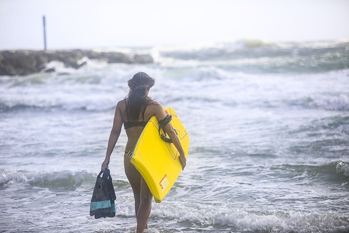 a woman going to the ocean while carrying a bodyboard on a leash and swim fins