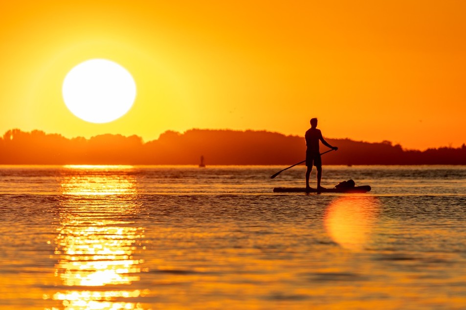 Stand-up paddleboarding with the sunset, a man facing the sunset, ocean