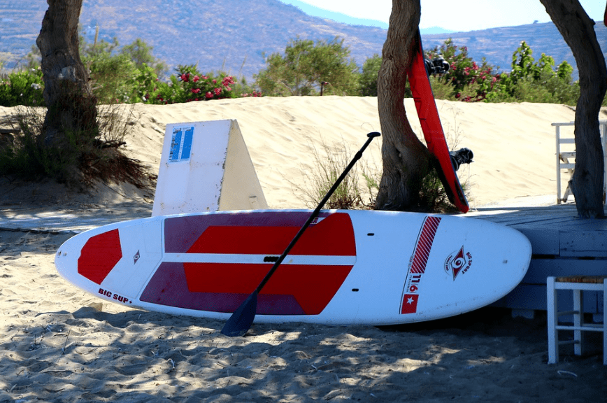 single paddleboard, red and white in color, white sand