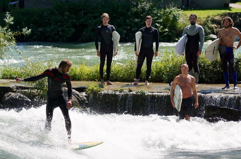 A group of surfers waiting for their turn at the riverbank while one is surfing