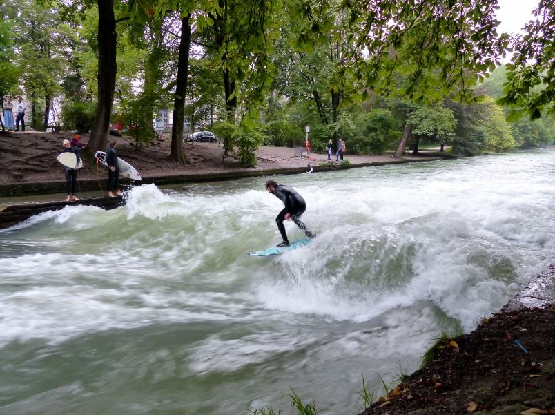 A man surfing in the river with other surfers and observers on the river banks