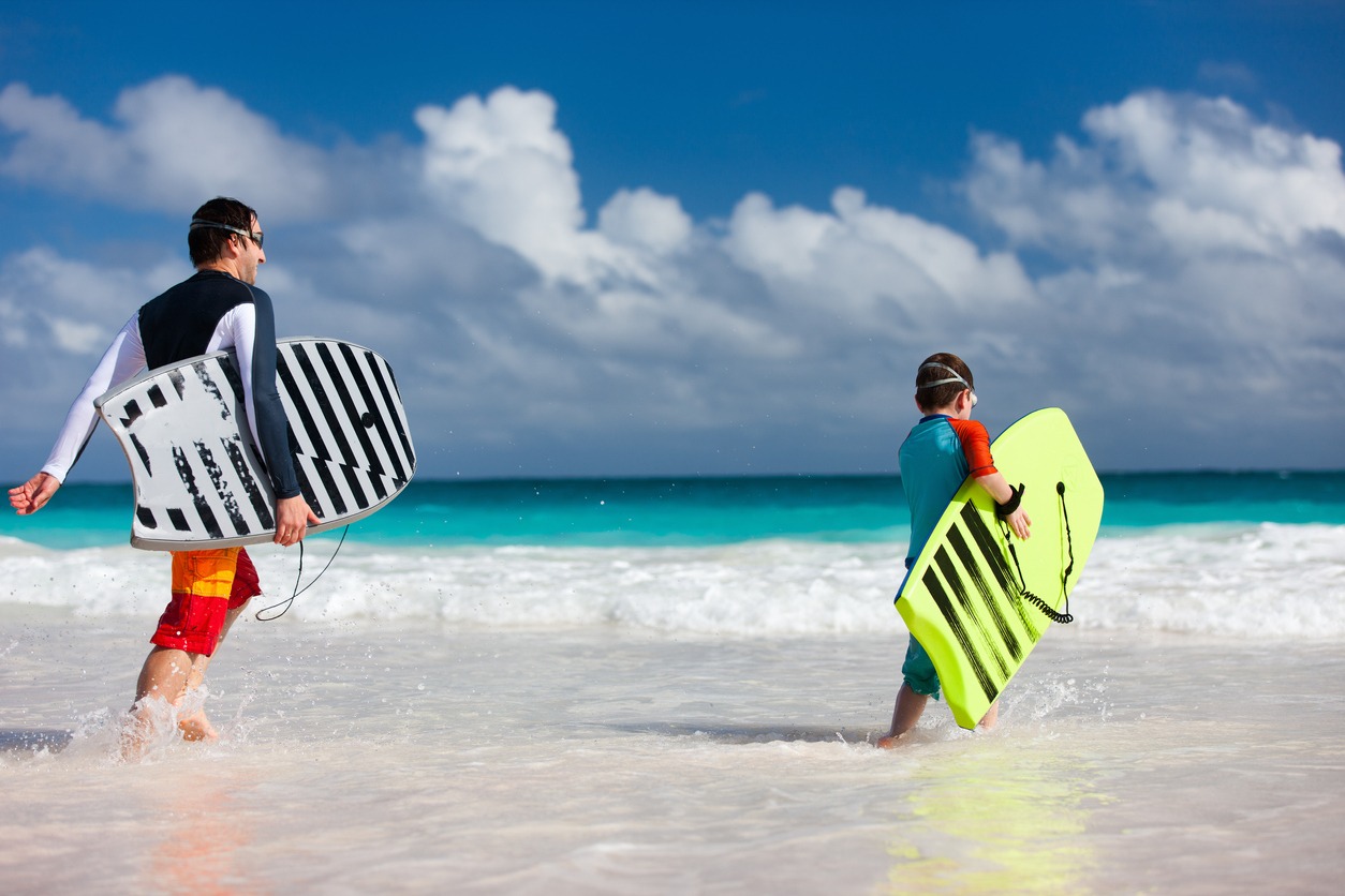 a father and son running towards ocean with boogie boards