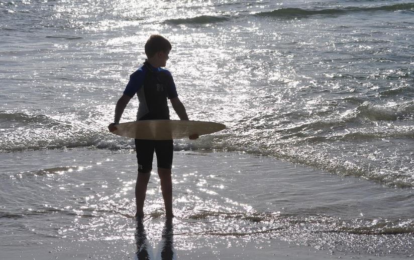 a silhouette of a boy holding a skimboard at the sea